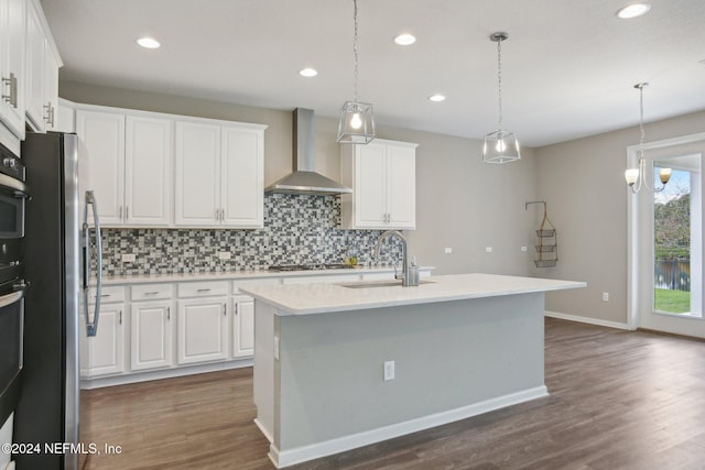 kitchen with wall chimney exhaust hood, a center island with sink, sink, and white cabinetry