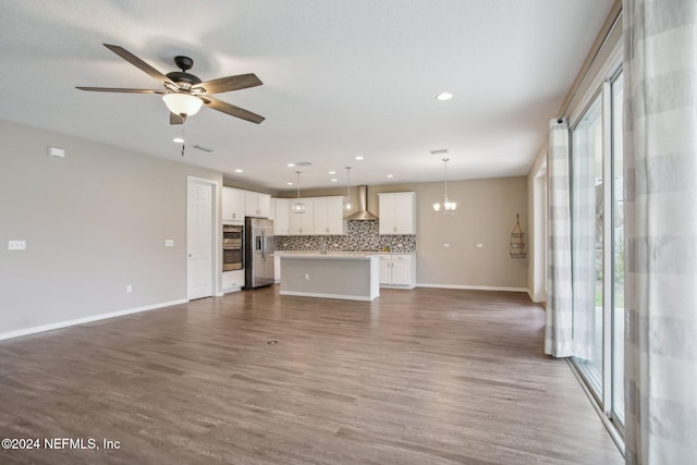 unfurnished living room featuring ceiling fan with notable chandelier, plenty of natural light, and hardwood / wood-style flooring