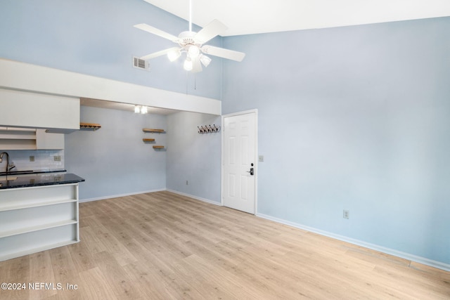 unfurnished living room featuring a high ceiling, light hardwood / wood-style flooring, ceiling fan, and sink