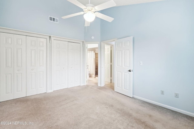 unfurnished bedroom with light colored carpet, high vaulted ceiling, ceiling fan, and multiple closets