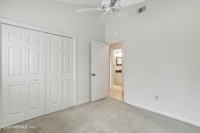 unfurnished bedroom featuring ceiling fan, light colored carpet, a towering ceiling, and a closet