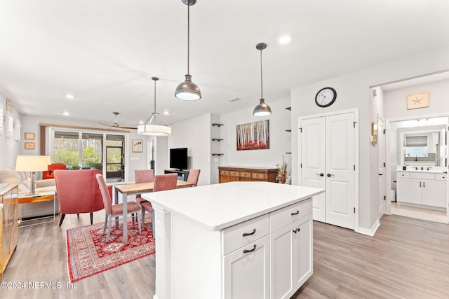 kitchen with white cabinets, decorative light fixtures, light hardwood / wood-style floors, and a kitchen island