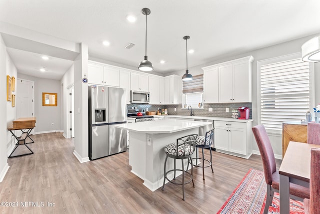 kitchen featuring appliances with stainless steel finishes, light wood-type flooring, decorative light fixtures, a center island, and white cabinetry