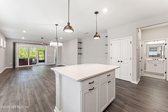 kitchen with light countertops, a kitchen island, baseboards, open floor plan, and dark wood-style flooring