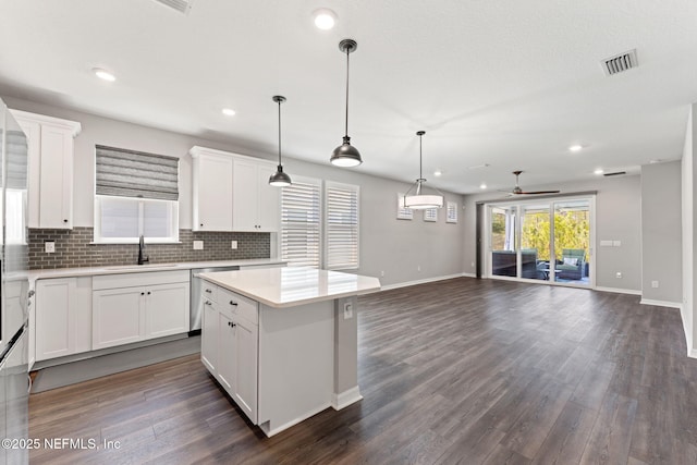 kitchen with a sink, ceiling fan, backsplash, baseboards, and visible vents
