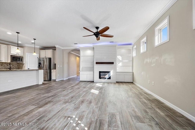 unfurnished living room with wood-type flooring, a large fireplace, ceiling fan, and crown molding