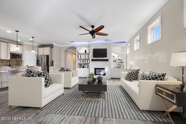 living room with a fireplace, dark hardwood / wood-style flooring, ornamental molding, ceiling fan, and a textured ceiling