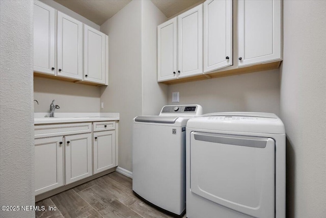 laundry area featuring cabinets, separate washer and dryer, sink, and light wood-type flooring