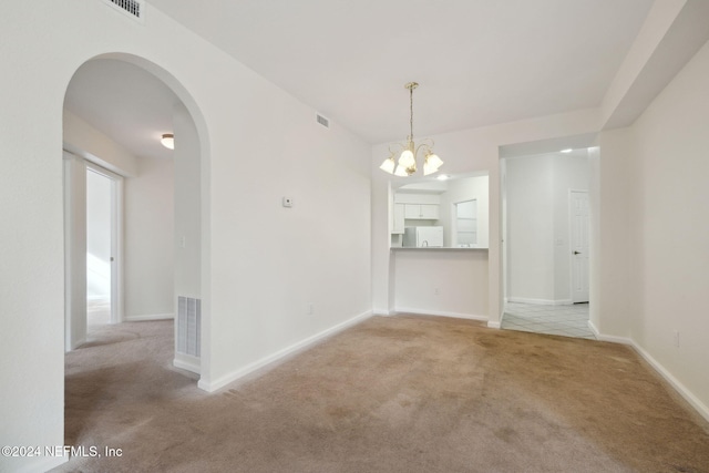 spare room featuring a chandelier and light colored carpet