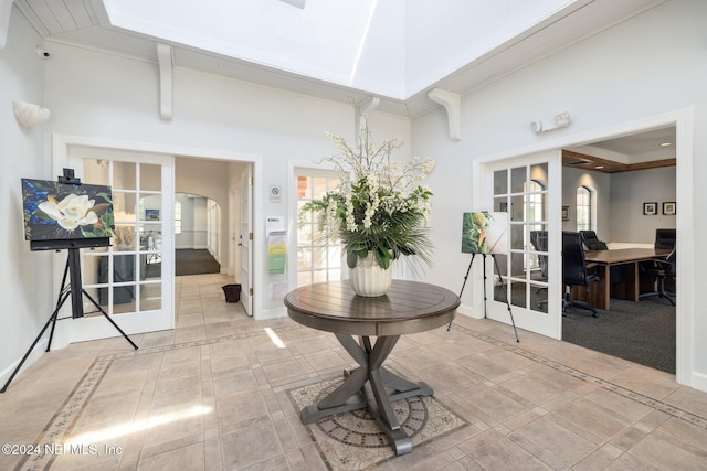 foyer entrance with tile patterned flooring, ornamental molding, a high ceiling, and french doors