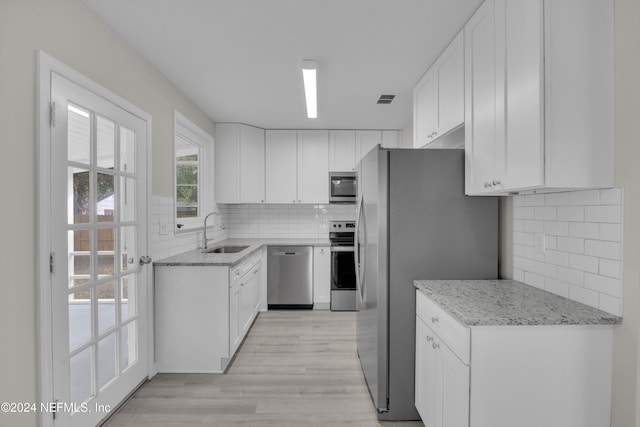 kitchen with light stone countertops, stainless steel appliances, sink, light hardwood / wood-style floors, and white cabinetry