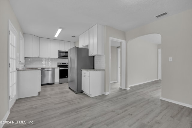 kitchen with backsplash, white cabinets, light wood-type flooring, a textured ceiling, and appliances with stainless steel finishes