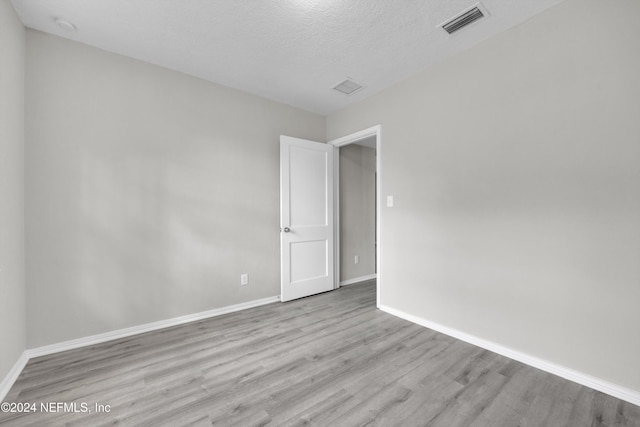 spare room with a textured ceiling and light hardwood / wood-style floors