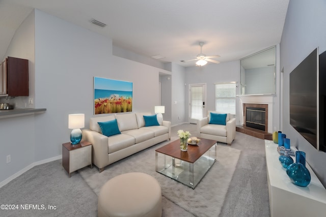 living room with a tile fireplace, light carpet, and ceiling fan