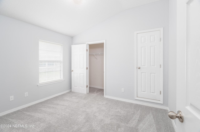 unfurnished bedroom featuring a walk in closet, light colored carpet, and lofted ceiling