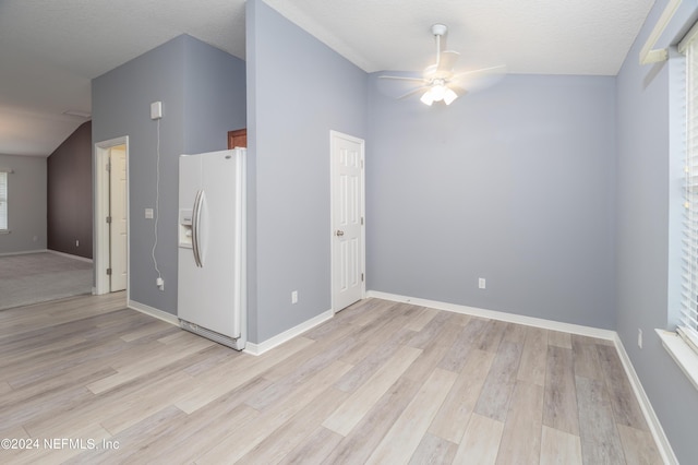 empty room featuring ceiling fan, light wood-type flooring, a textured ceiling, and lofted ceiling