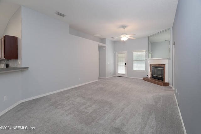 unfurnished living room with ceiling fan, light colored carpet, and a fireplace