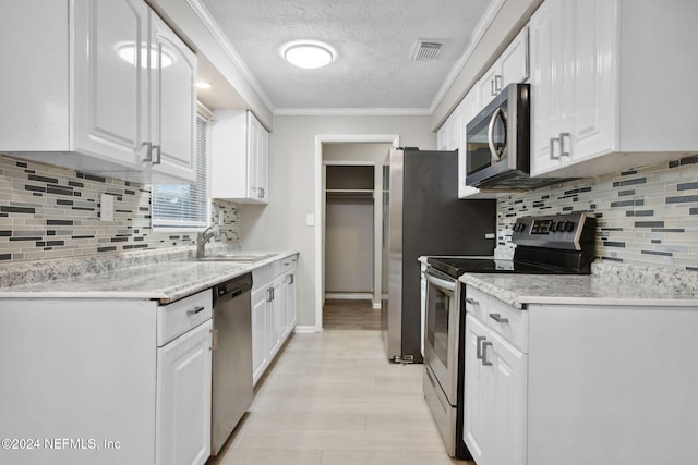 kitchen with white cabinets, sink, crown molding, a textured ceiling, and stainless steel appliances