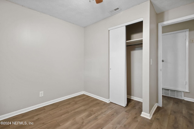 unfurnished bedroom featuring ceiling fan, a closet, wood-type flooring, and a textured ceiling