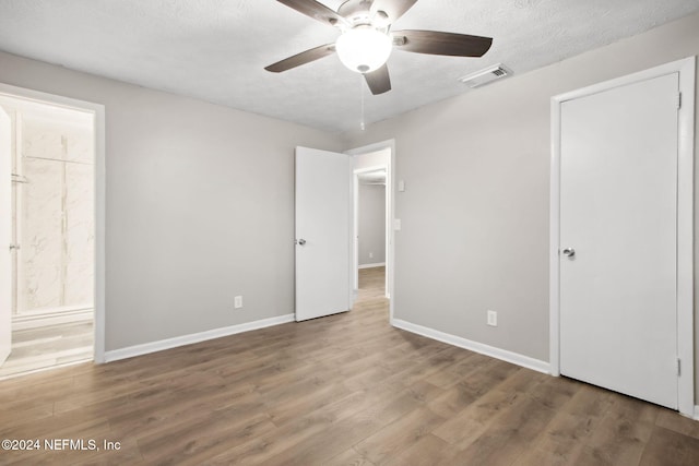 unfurnished bedroom with hardwood / wood-style floors, ensuite bathroom, ceiling fan, and a textured ceiling