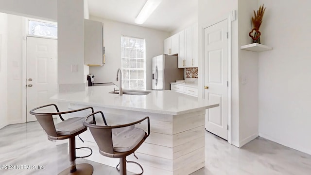 kitchen with a kitchen bar, stainless steel refrigerator with ice dispenser, kitchen peninsula, and white cabinetry