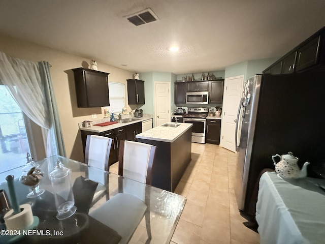 kitchen with a center island with sink, sink, light tile patterned floors, and stainless steel appliances