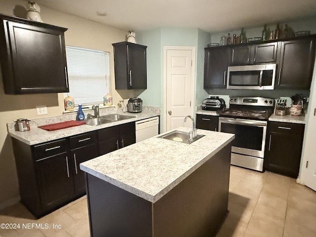 kitchen with light tile patterned floors, stainless steel appliances, a kitchen island with sink, and sink