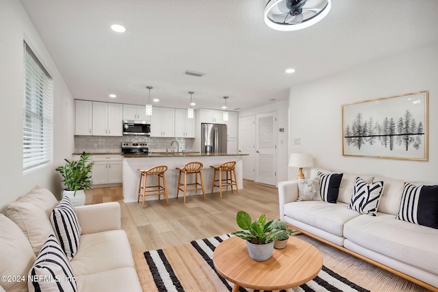 living room with light hardwood / wood-style floors, ceiling fan, and sink