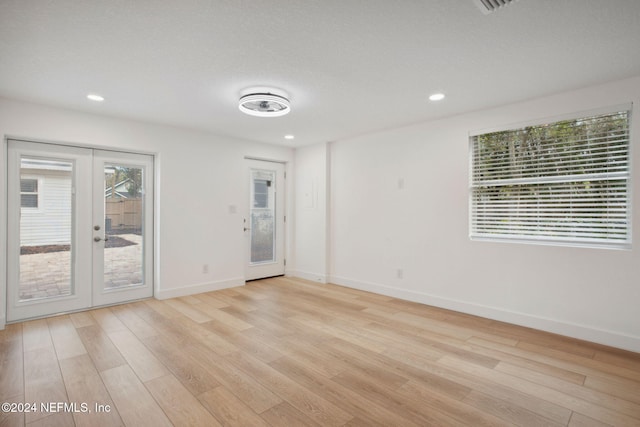 empty room with a wealth of natural light, french doors, a textured ceiling, and light wood-type flooring