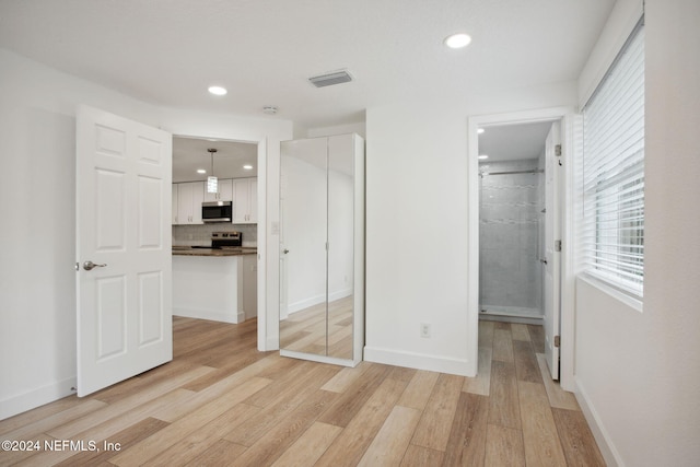 unfurnished bedroom with light wood-type flooring, ensuite bath, and a closet