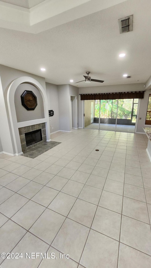 unfurnished living room featuring ceiling fan, light tile patterned floors, and a tiled fireplace