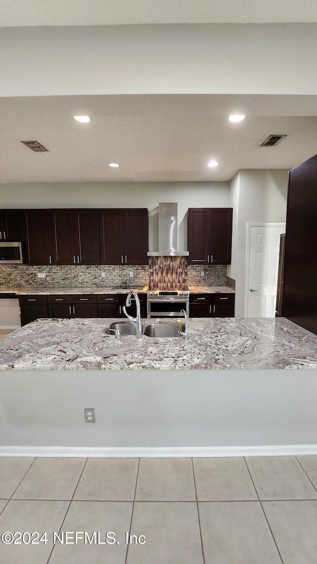 kitchen featuring sink, wall chimney exhaust hood, stainless steel appliances, light stone counters, and backsplash