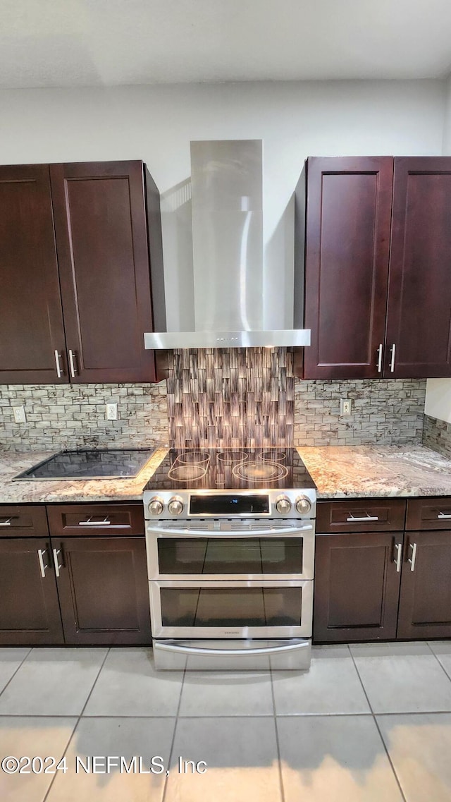 kitchen with light stone countertops, range with two ovens, wall chimney range hood, and backsplash