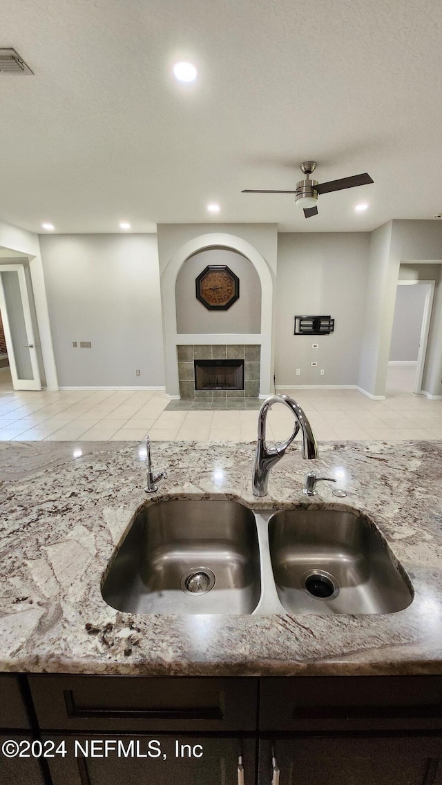 kitchen featuring light stone counters, ceiling fan, sink, a fireplace, and light tile patterned flooring