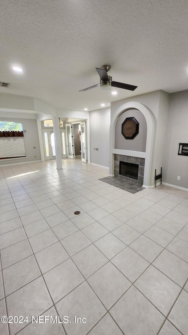 unfurnished living room with light tile patterned flooring, a textured ceiling, ceiling fan, and a tiled fireplace