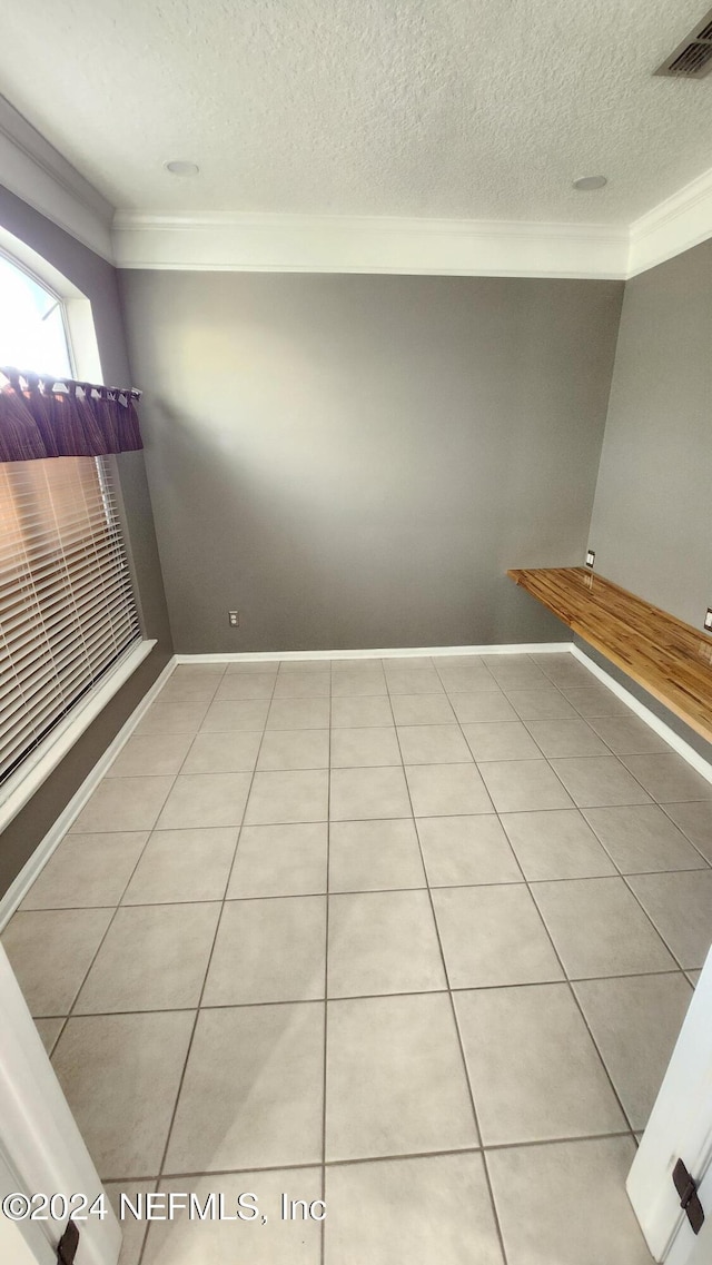 unfurnished room featuring light tile patterned floors, a textured ceiling, and ornamental molding