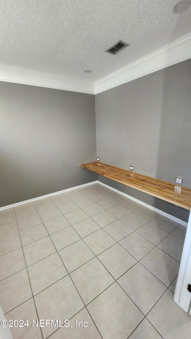 tiled empty room featuring ornamental molding and a textured ceiling