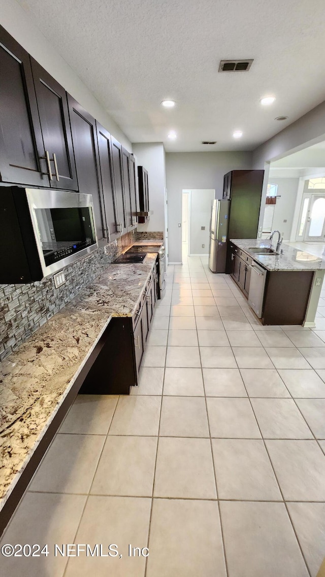 kitchen featuring appliances with stainless steel finishes, light stone counters, a textured ceiling, sink, and light tile patterned floors