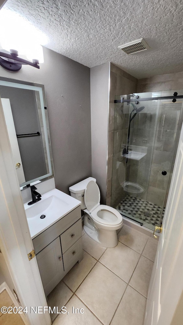 bathroom featuring tile patterned flooring, a textured ceiling, toilet, and walk in shower