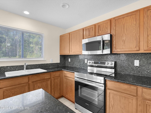 kitchen featuring sink, stainless steel appliances, backsplash, dark stone countertops, and light tile patterned floors