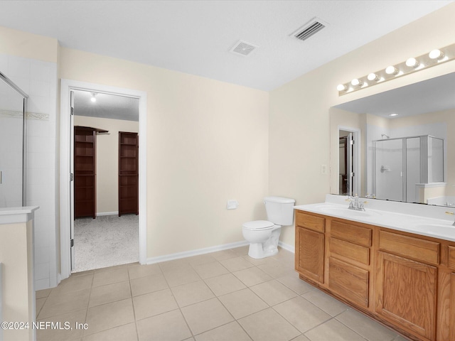 bathroom featuring tile patterned flooring, vanity, a shower with shower door, and toilet