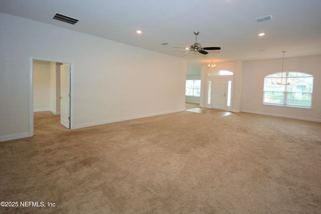 unfurnished living room featuring ceiling fan with notable chandelier, light carpet, and a wealth of natural light