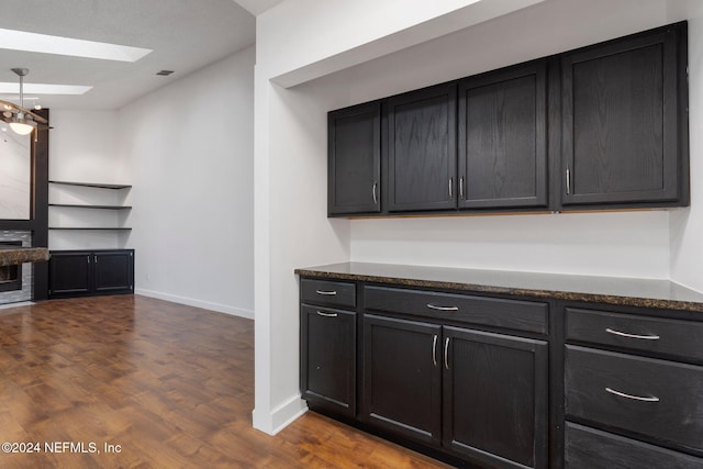 kitchen with a skylight, an inviting chandelier, dark stone counters, and hardwood / wood-style flooring