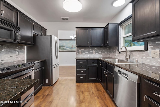 kitchen with backsplash, sink, light hardwood / wood-style flooring, dark stone countertops, and stainless steel appliances