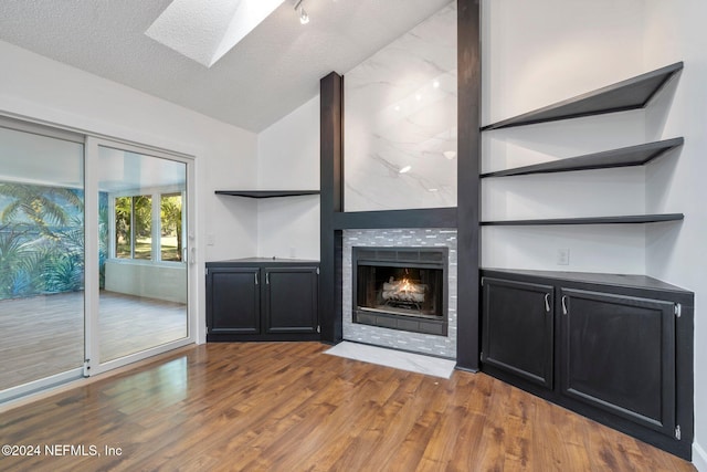 unfurnished living room with a fireplace, hardwood / wood-style floors, a textured ceiling, and vaulted ceiling with skylight