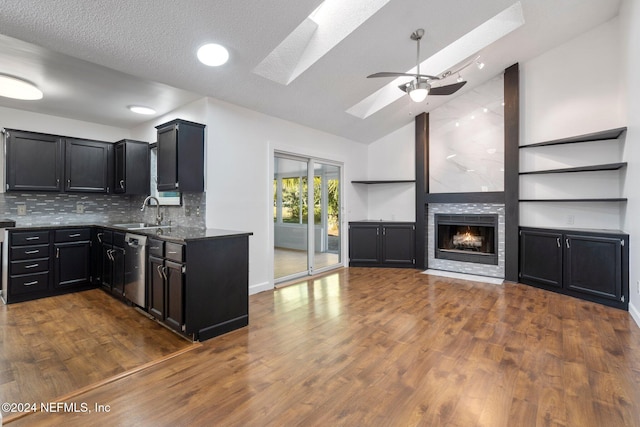 kitchen featuring dishwasher, lofted ceiling with skylight, sink, dark hardwood / wood-style floors, and a fireplace