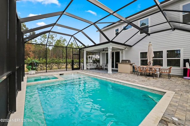 view of swimming pool with a patio, glass enclosure, ceiling fan, and exterior kitchen