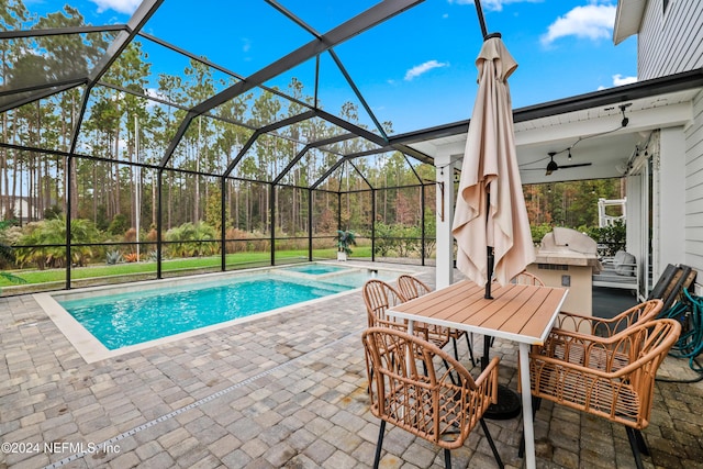 view of swimming pool with glass enclosure, ceiling fan, a patio, and an outdoor kitchen