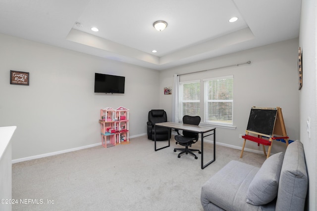 office area with a raised ceiling and light carpet