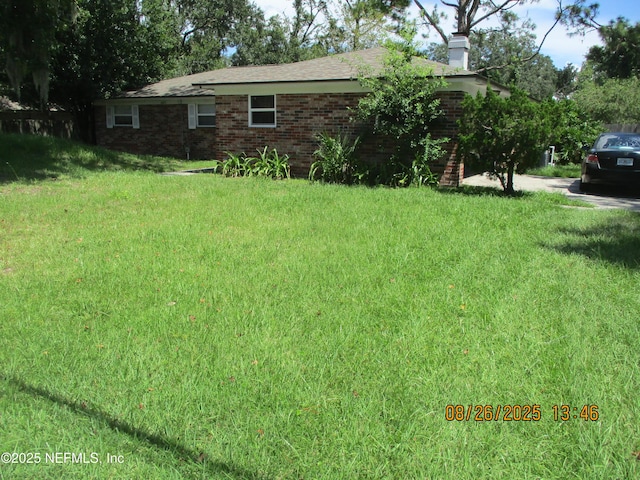 exterior space featuring brick siding, a chimney, and a front lawn